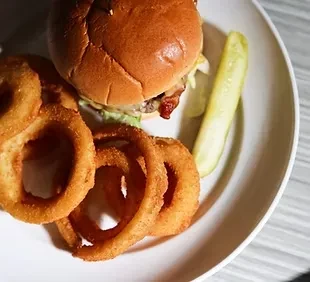 A classic burger, crispy onion rings, and a dill pickle spear.
