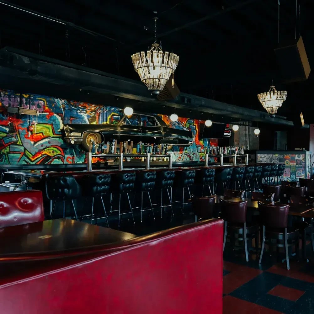Bar interior features a mounted black car above colorful graffiti.