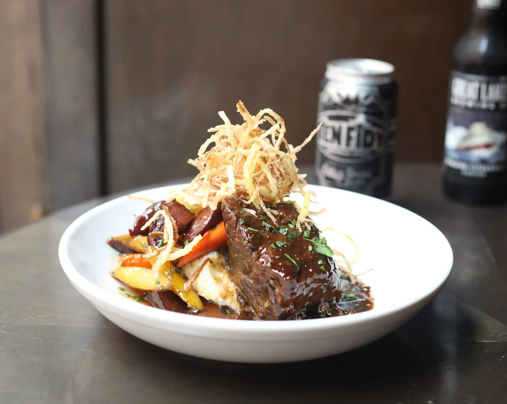 Braised meat with mashed potatoes, roasted vegetables, and crispy topping.