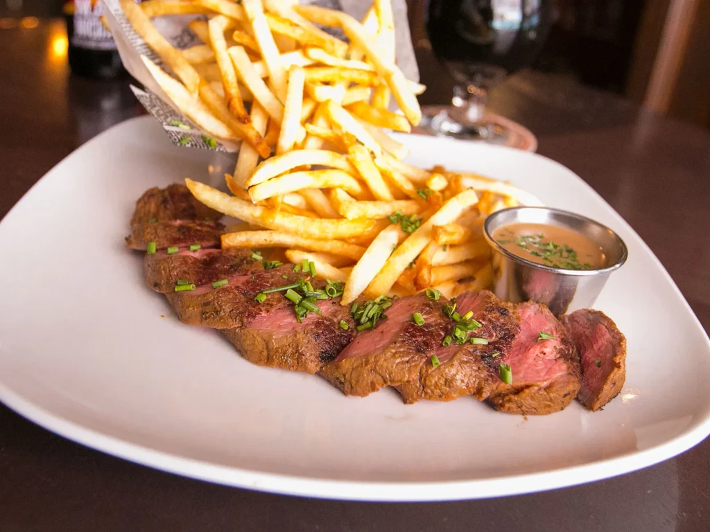 Sliced medium-rare steak topped with chives, golden fries, and dipping sauce.