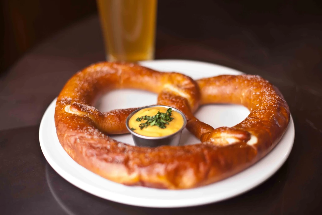 Golden-brown soft pretzel with coarse salt, cheese dip, and beer.