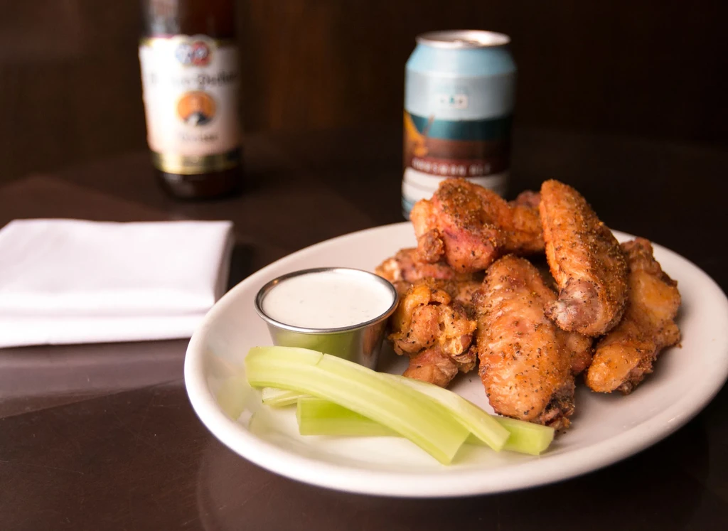 Golden-brown chicken wings with celery, creamy dip, and drinks.