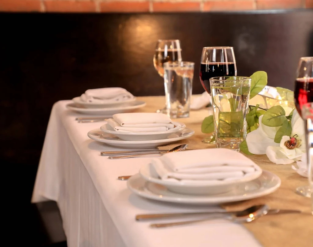 Restaurant table with place settings, wine glasses, and floral centerpiece.