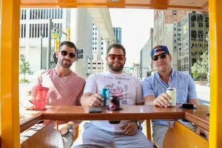 Smiling men in sunglasses hold drinks on a city mobile bar.
