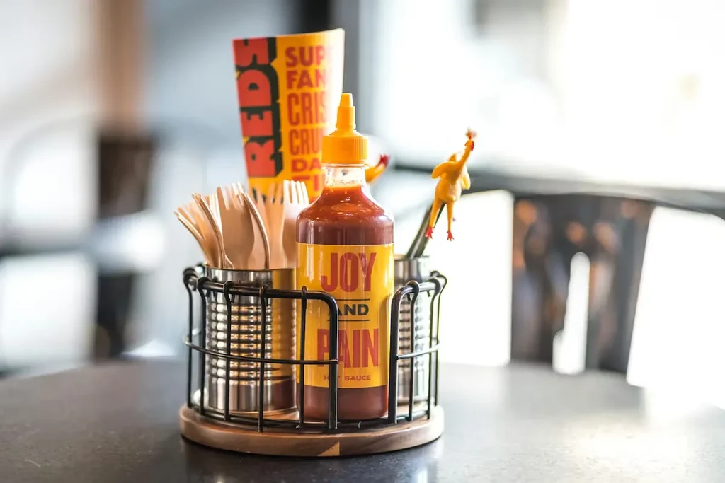 Black wire caddy with forks, Joy and Pain Hot Sauce, rubber chicken.