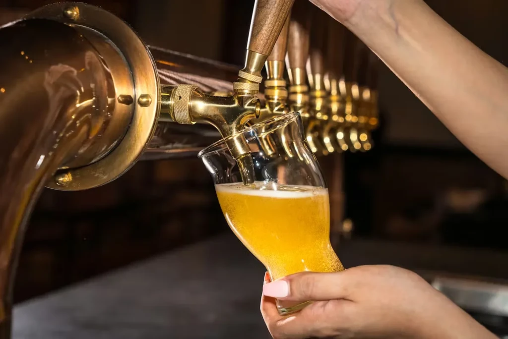 A hand fills a glass with golden beer from a brass tap.