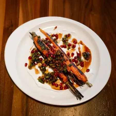 Plated roasted carrots with herbs, pomegranate, and dark sauce.