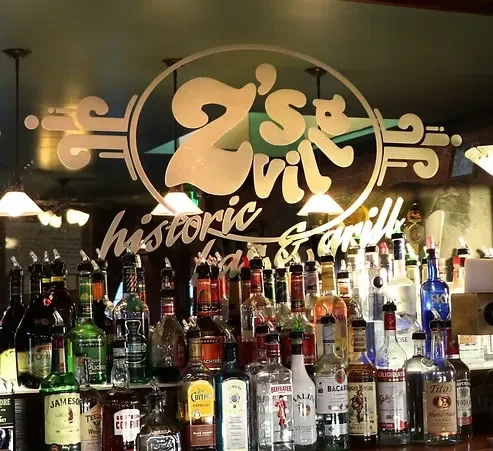 Well-stocked bar shelves with bottles and Z's Vil historic & Grill sign.
