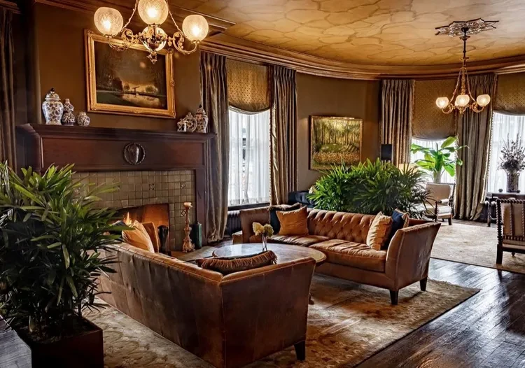 Luxurious room with tufted leather sofas, a fireplace, and a gilded ceiling.