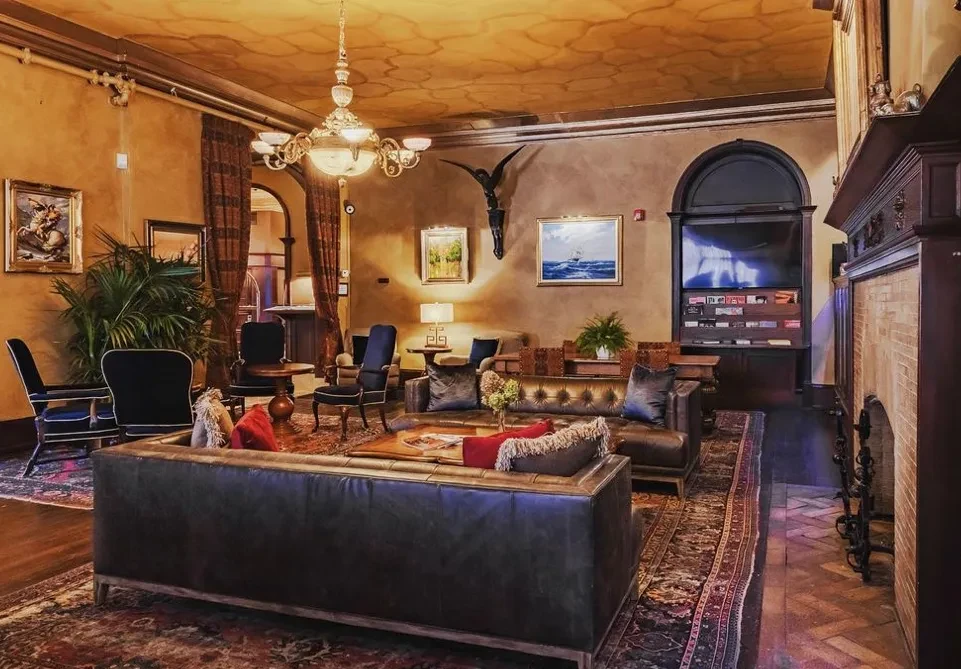 Elegant lounge with leather sofas, ornate chandelier, patterned rug, and artwork.