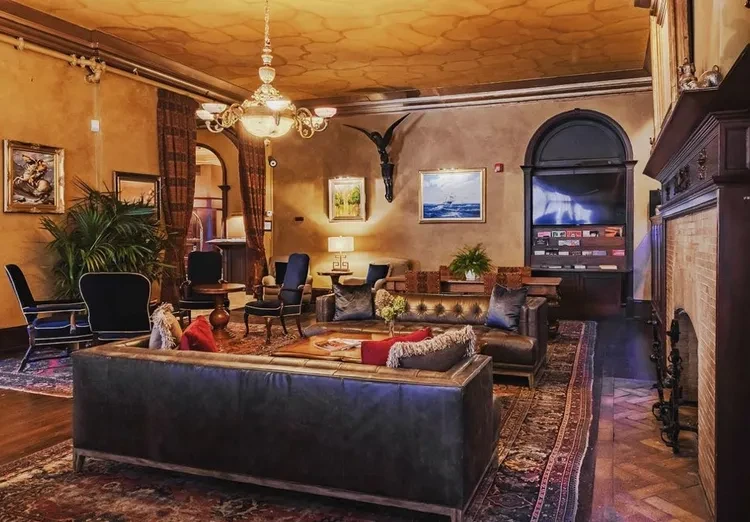Luxurious lounge with ornate chandelier, sofa, fireplace, and framed artwork.