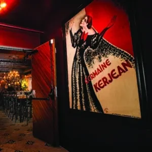 Vintage Romaine Kerjean poster in dimly lit restaurant entrance with open door.