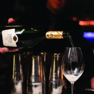 Hand pouring COMTE'S sparkling wine into a glass at a dim bar.