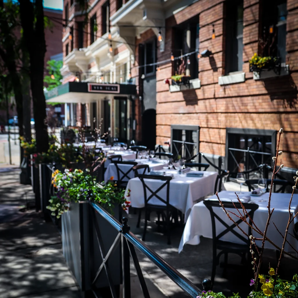 Sunny outdoor restaurant patio with set tables and X-back chairs.