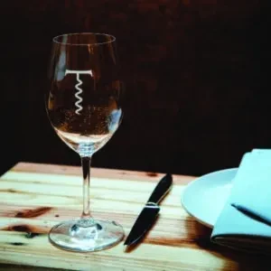 Empty wine glass with corkscrew etching on a wooden table setting.