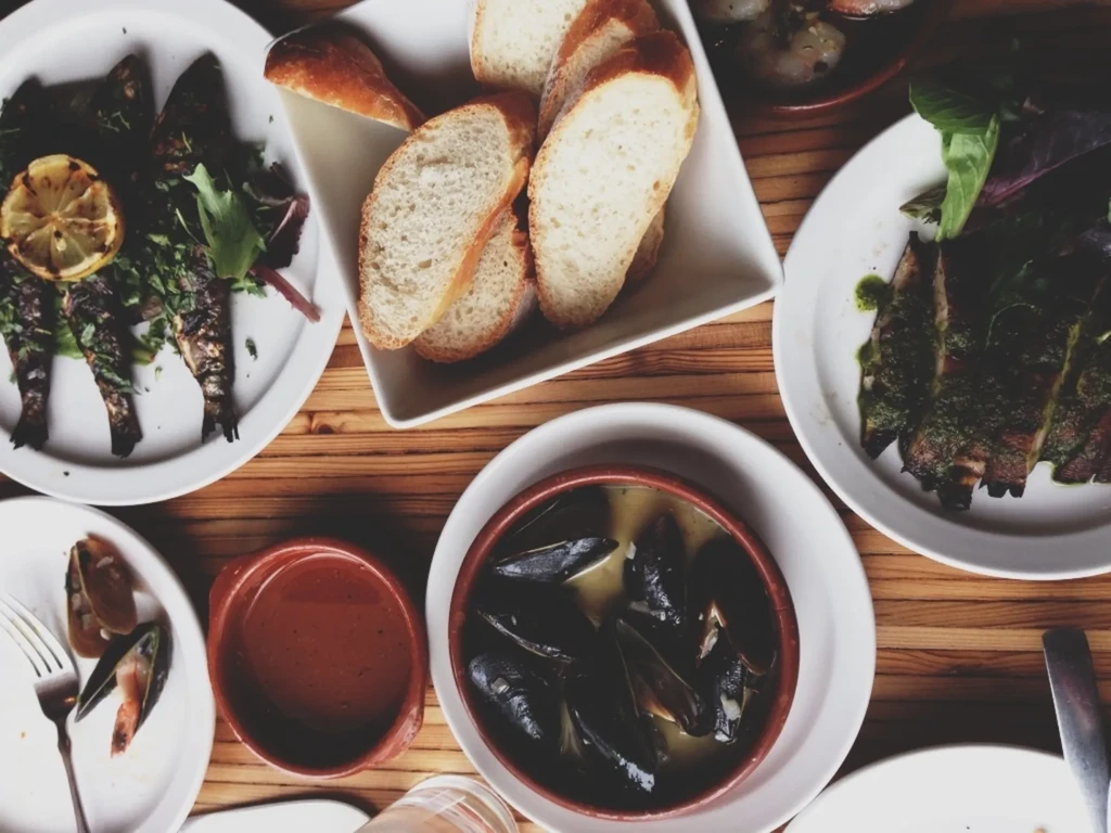 Overhead view of rustic table with grilled fish, mussels, meat, and bread.