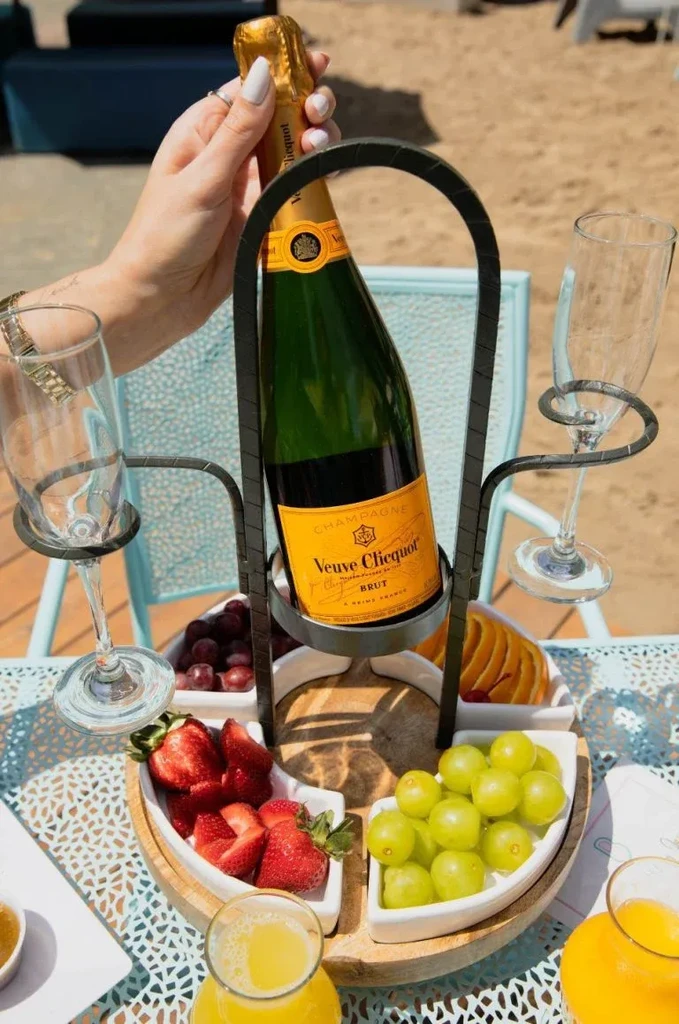 A hand holds a champagne bottle among flutes, fruit, and orange juice.