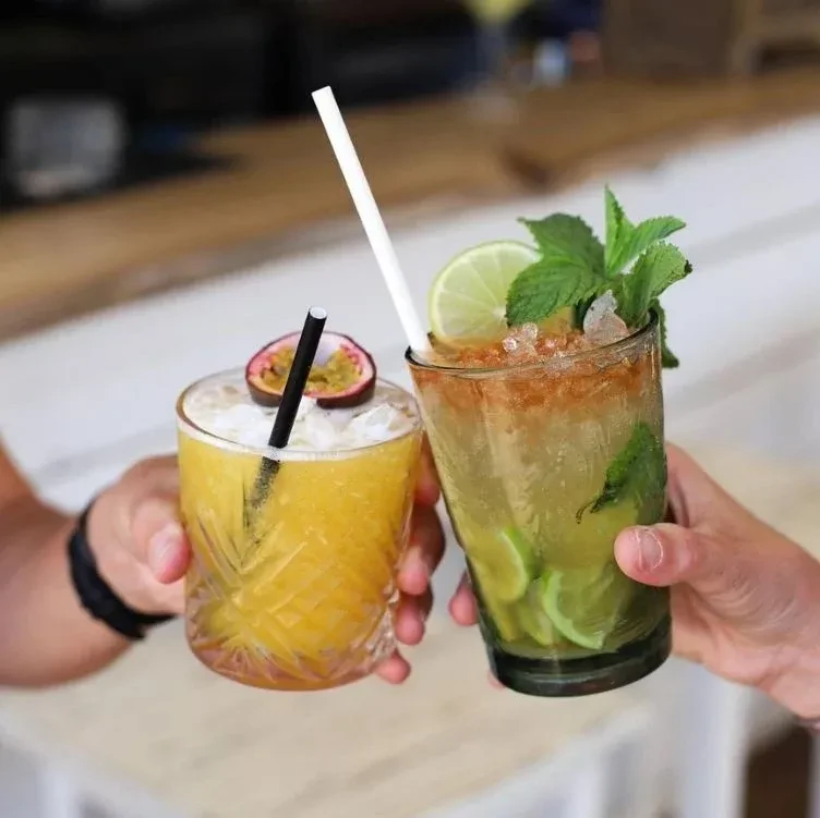 Two hands hold a yellow passion fruit and a green lime cocktail.