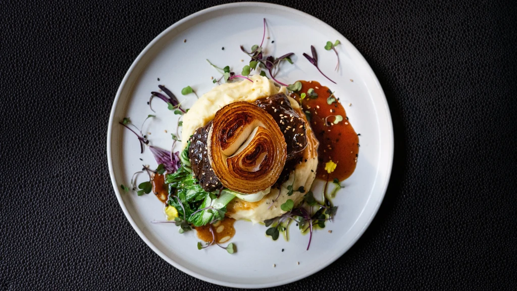 Plated short rib, mashed potatoes, fanned caramelized onion, greens, sauce.