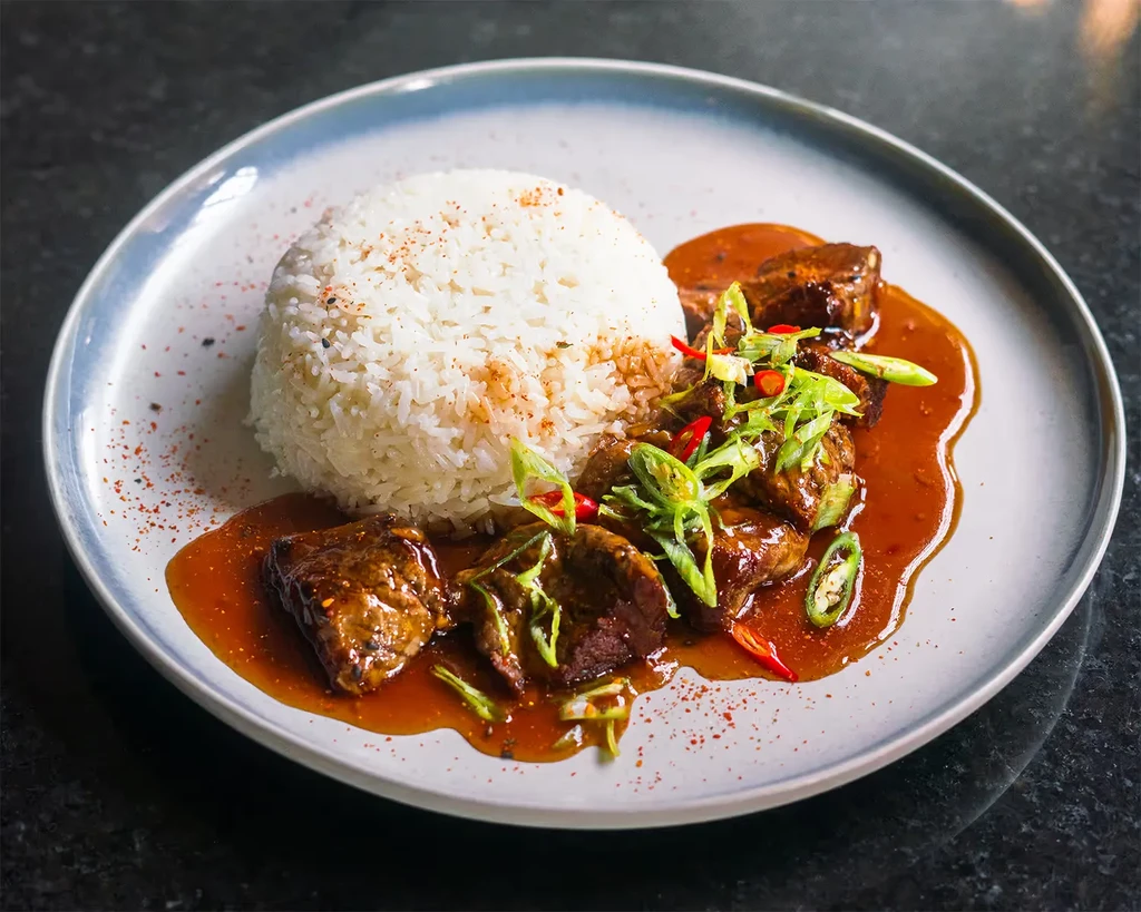 A well-plated dish of spiced rice, glazed meat, and vibrant garnishes.