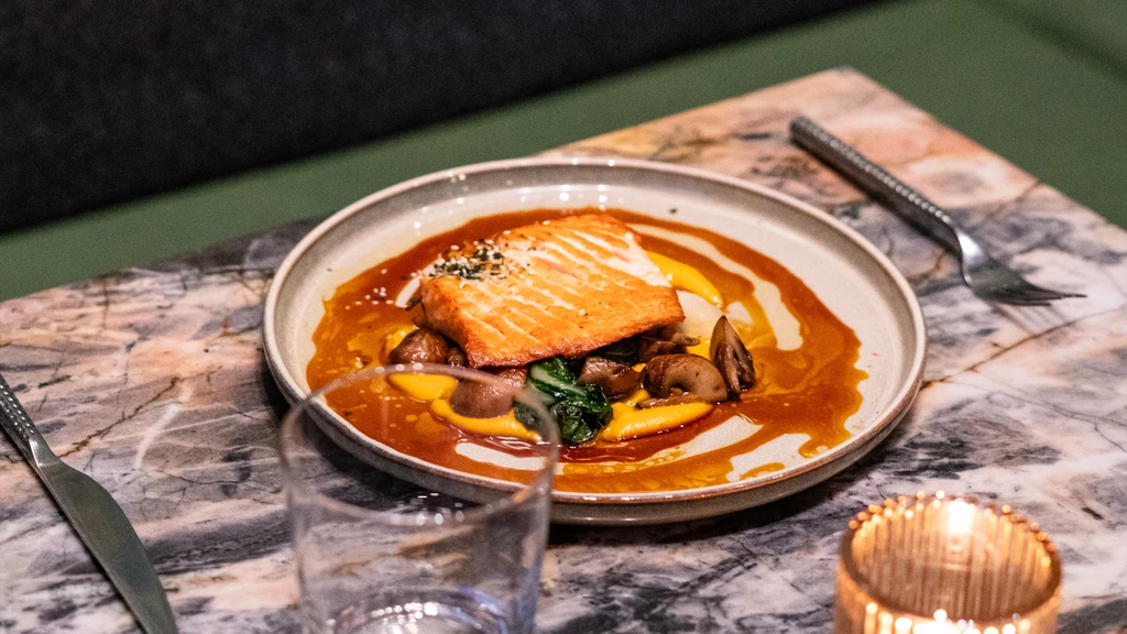 Pan-seared salmon, yellow purée, greens, and sauce on a marbled table.