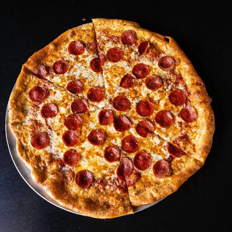 Freshly baked pepperoni pizza with herbs, sliced, on a silver pan.