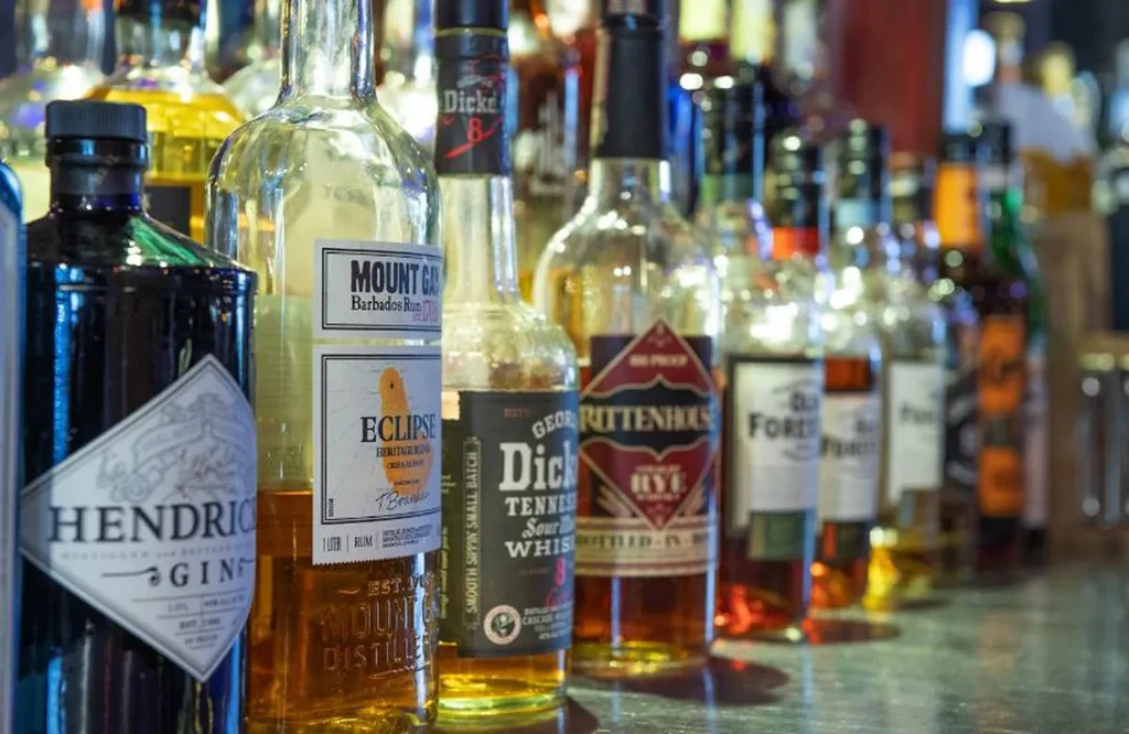 Hendrick's Gin, rum, whiskey, and rye bottles on a bar.