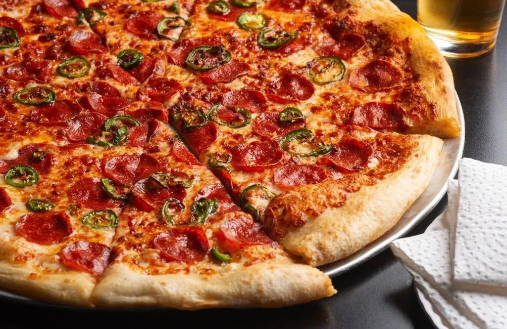 Sliced pepperoni and jalapeño pizza on a metal pan.