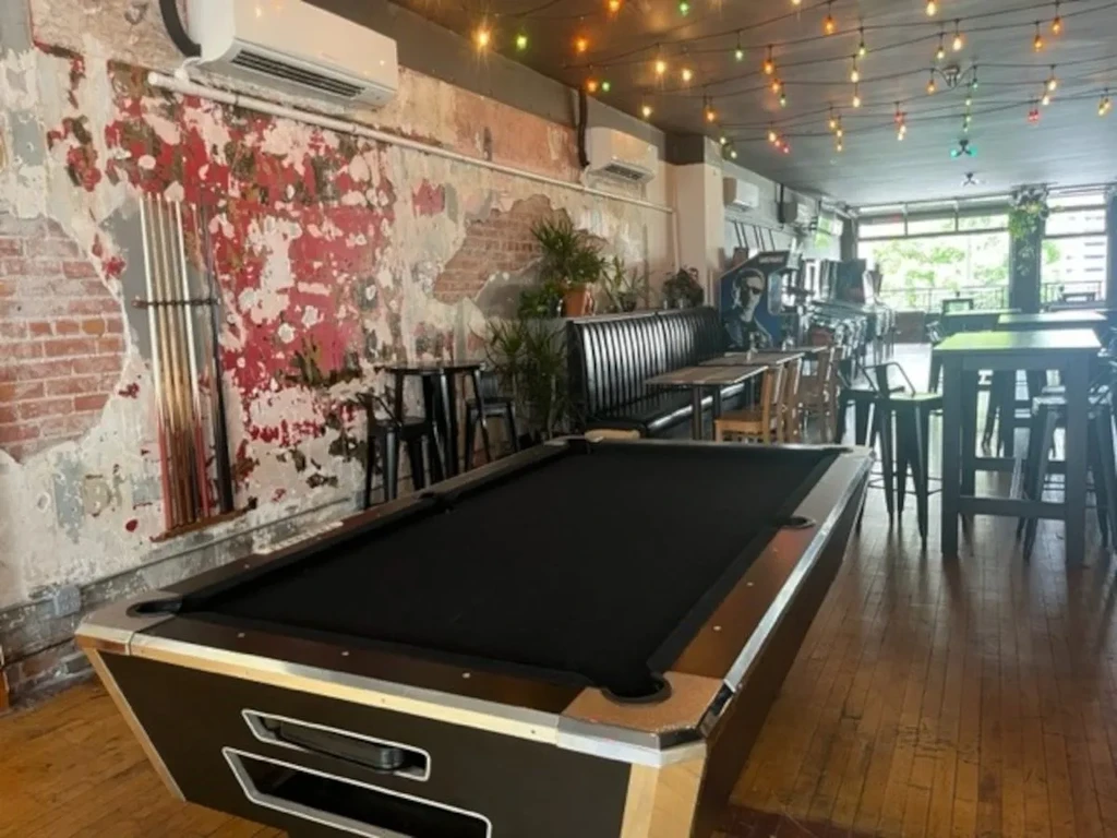 An empty bar interior with a black pool table and festive string lights.