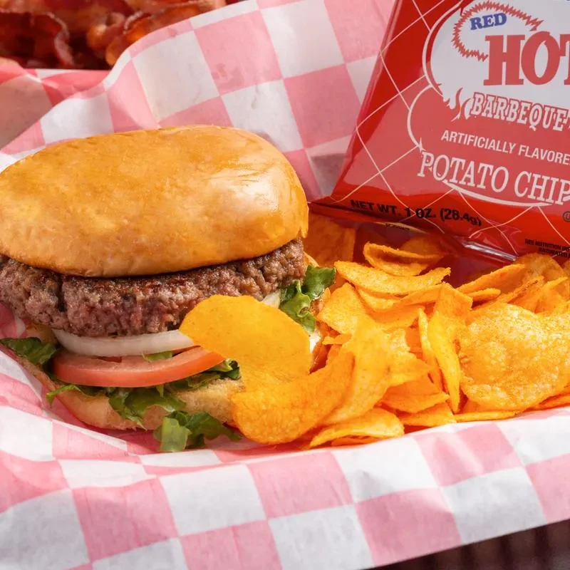 Close-up of a hamburger and Red Hot Barbeque chips on checkered paper.