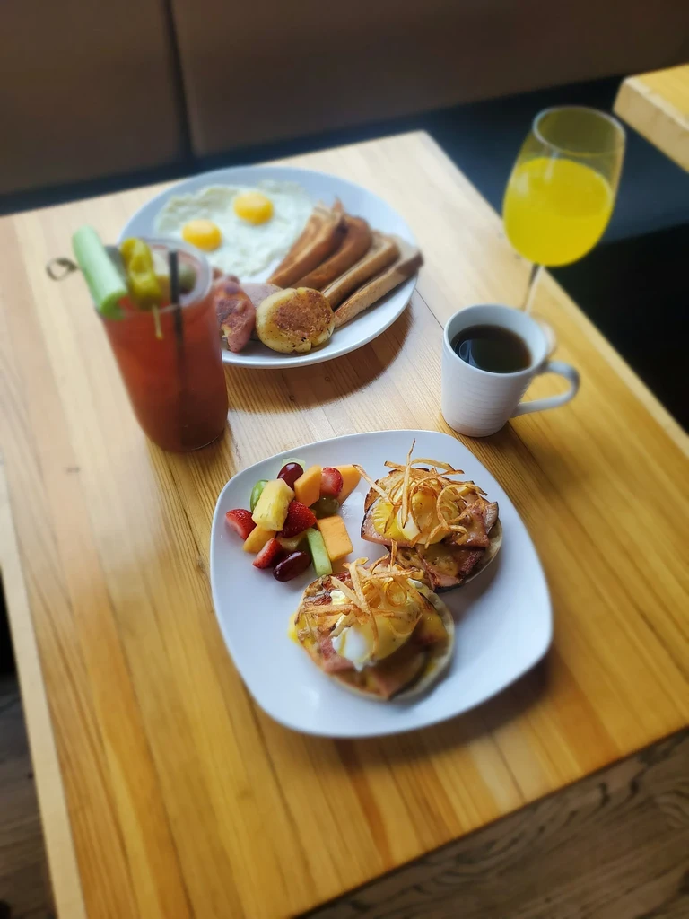 Overhead breakfast spread with eggs, bacon, Bloody Mary, Eggs Benedict, fruit.