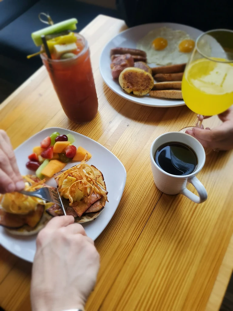 Hands cutting eggs Benedict at a top-down brunch spread.