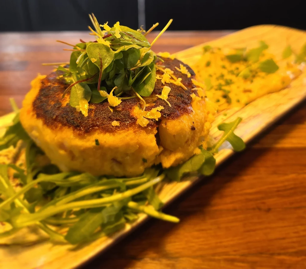 Golden seared patty, microgreens, arugula, and sauce on a wooden board.