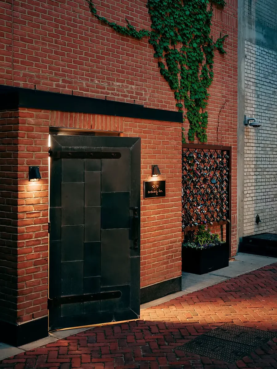 Brick alley entrance with black metal door and ivy-covered wall