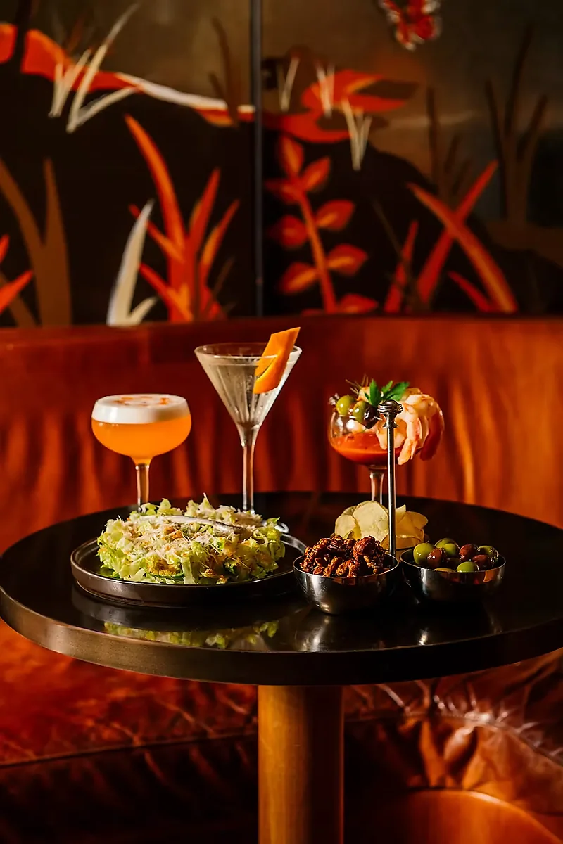 Two cocktails with shrimp cocktail, salad, nuts and olives on table
