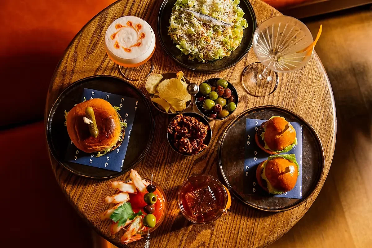 Overhead view of sliders, salad, olives, chips and three cocktails