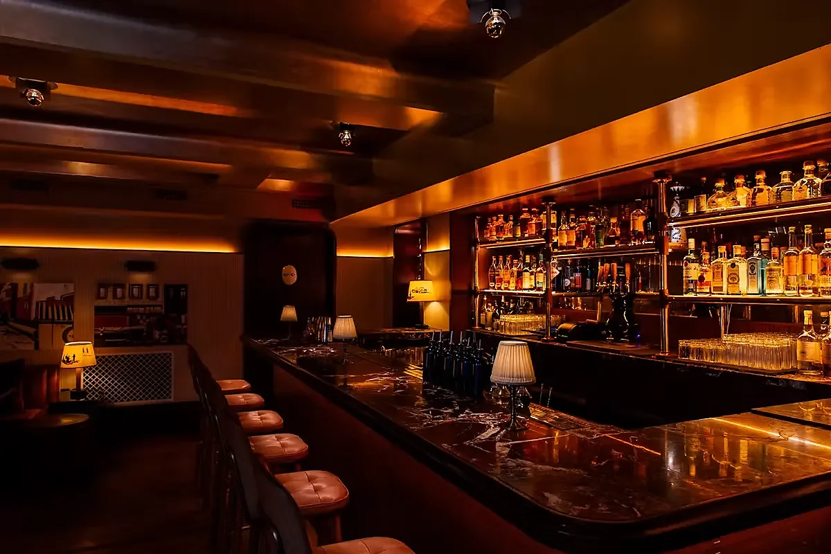 Dimly lit bar counter with leather stools and backlit liquor shelves