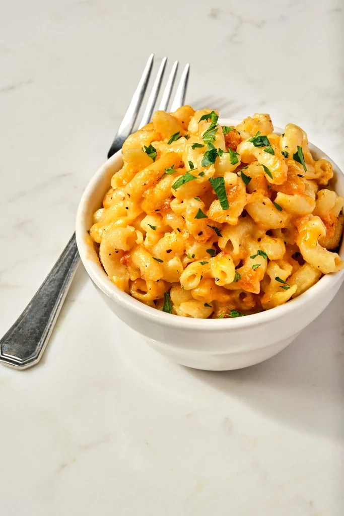Macaroni and cheese in a white bowl with herbs and a fork.