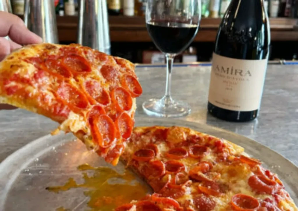 Hand lifts a pepperoni pizza slice, melted cheese and pooling grease.