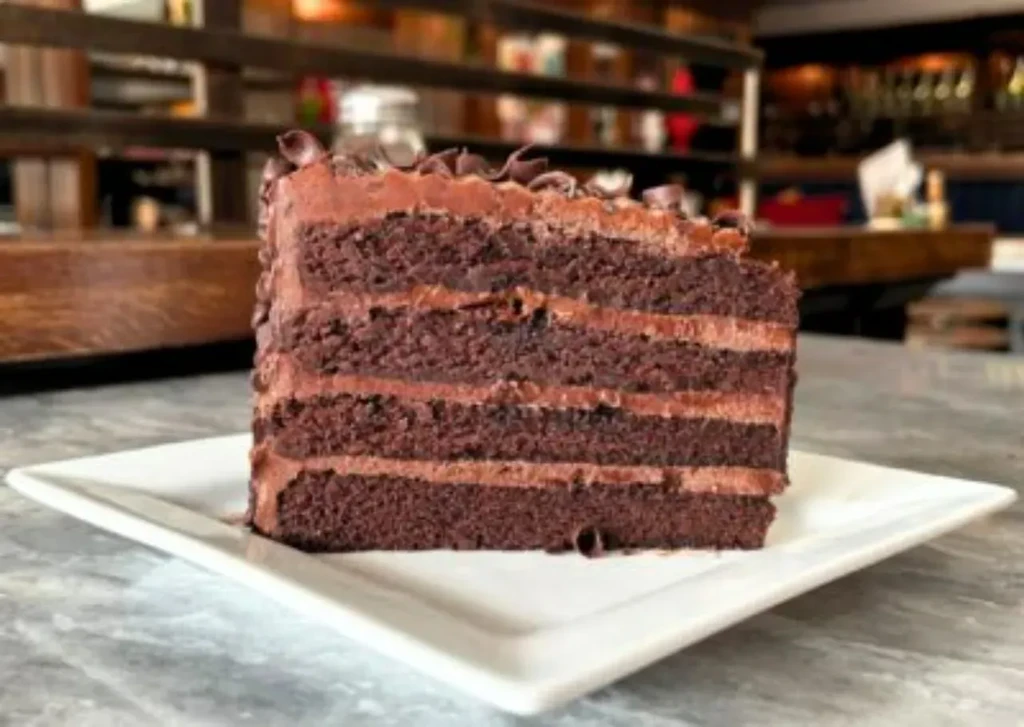 Layered chocolate cake slice with chocolate curls on a white plate.