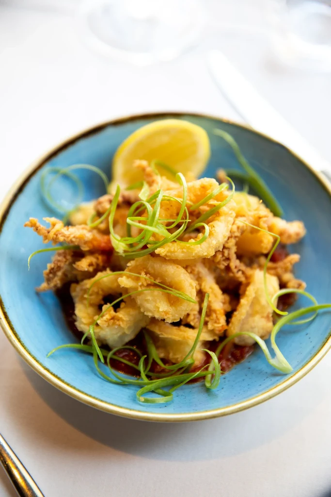Fried calamari with scallions, lemon, and sauce in a blue bowl.