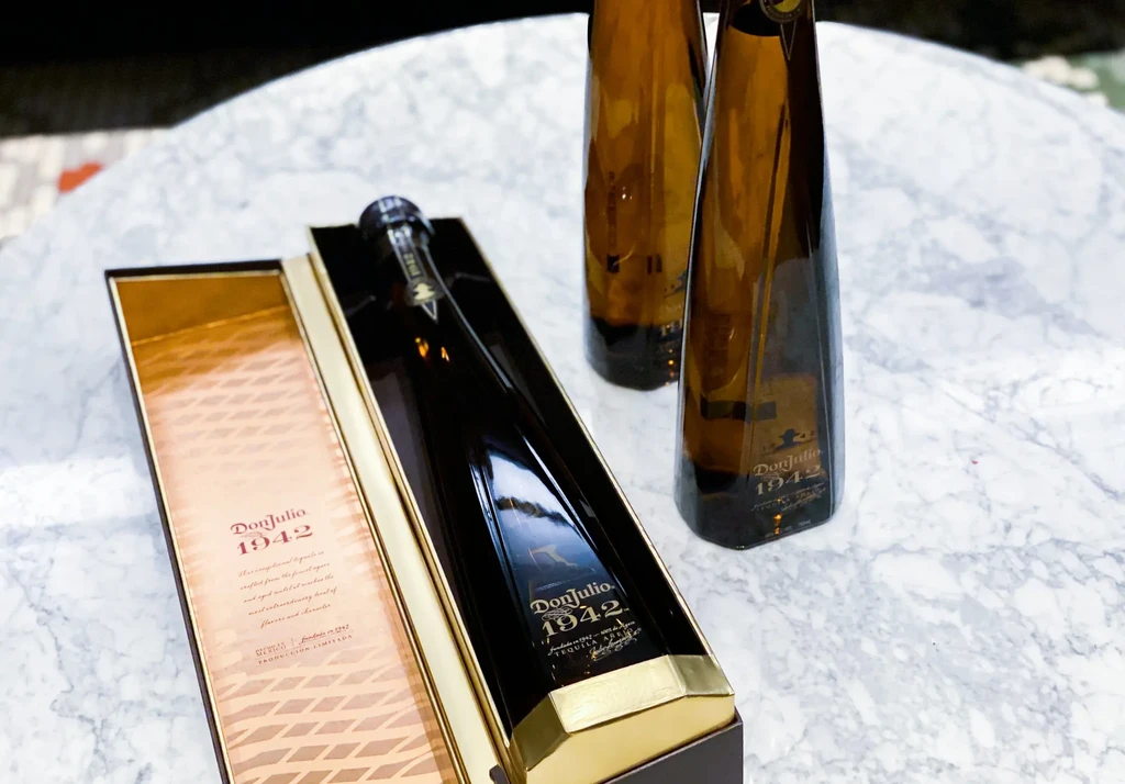 Three Don Julio 1942 tequila bottles, one boxed, on a marble surface.
