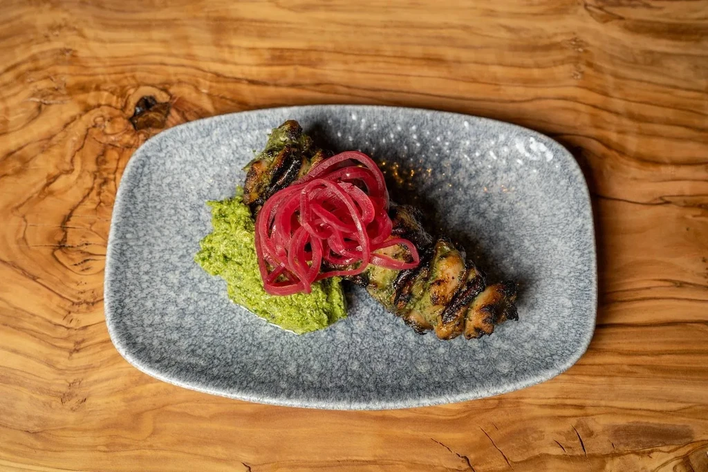 Grilled chicken with dark green herbs, red pickled onions, and green sauce.