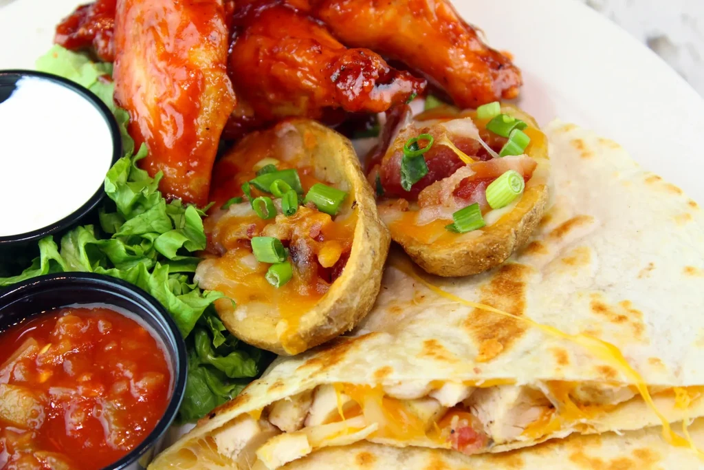 Platter of chicken wings, cheesy potato skins, and chicken quesadilla.