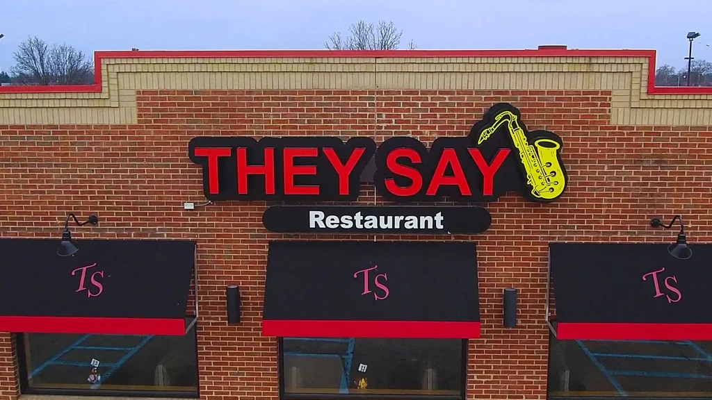 Red brick restaurant exterior with 'THEY SAY' sign and saxophone.