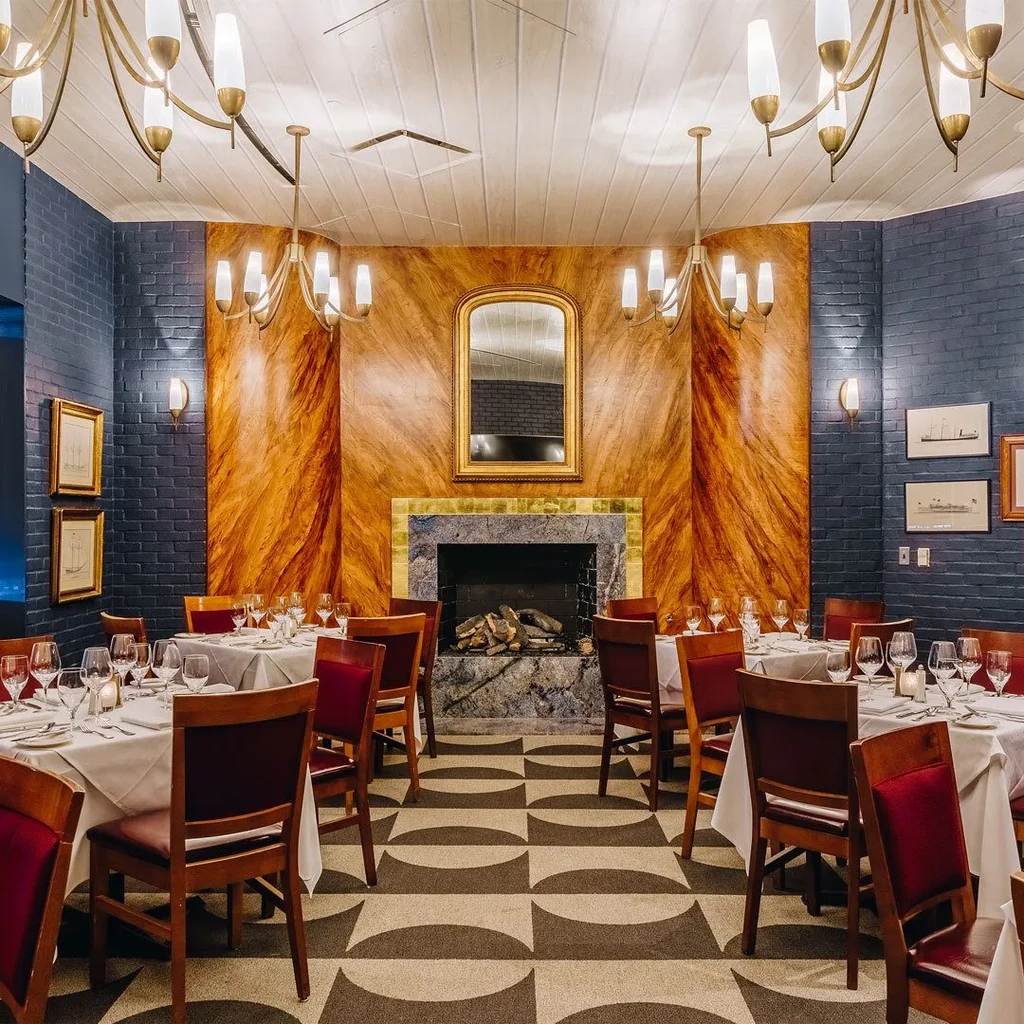 Elegant restaurant dining room with set tables, a fireplace, and blue brick walls.