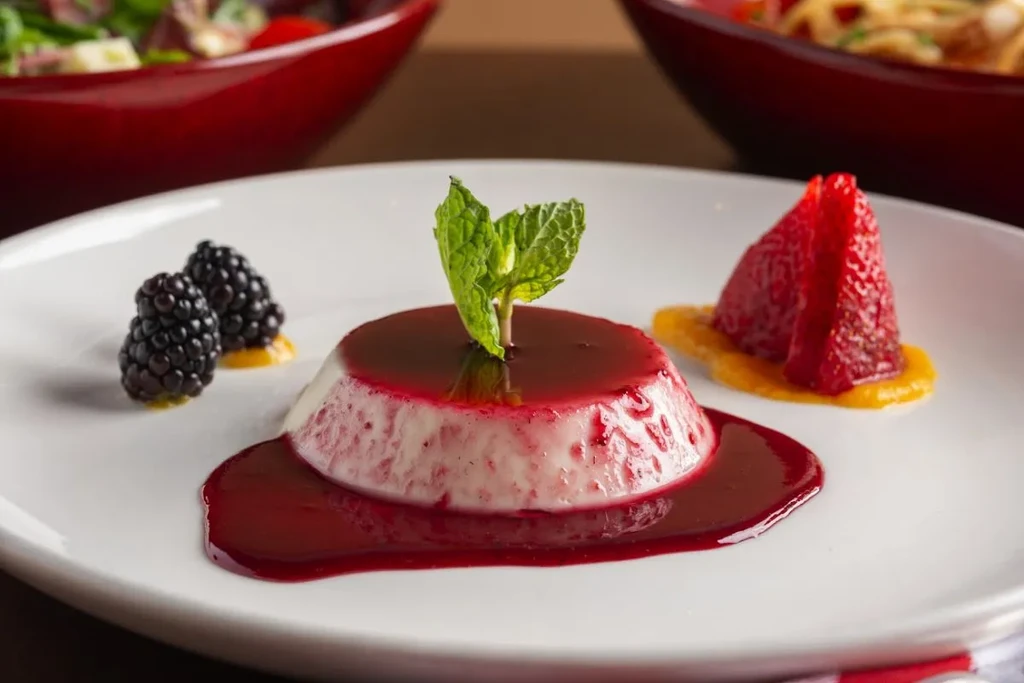 Plated dome dessert with berry sauce, mint, blackberries, and red fruit.