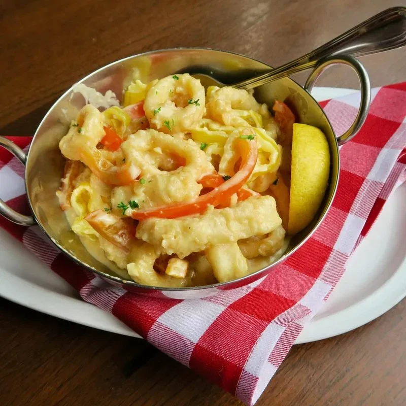 Fried calamari, peppers, lemon in steel bowl on checkered napkin.