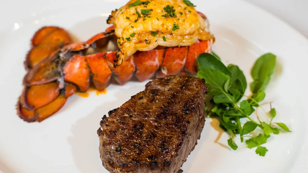 A cooked lobster tail and grilled steak with herbs on a plate.