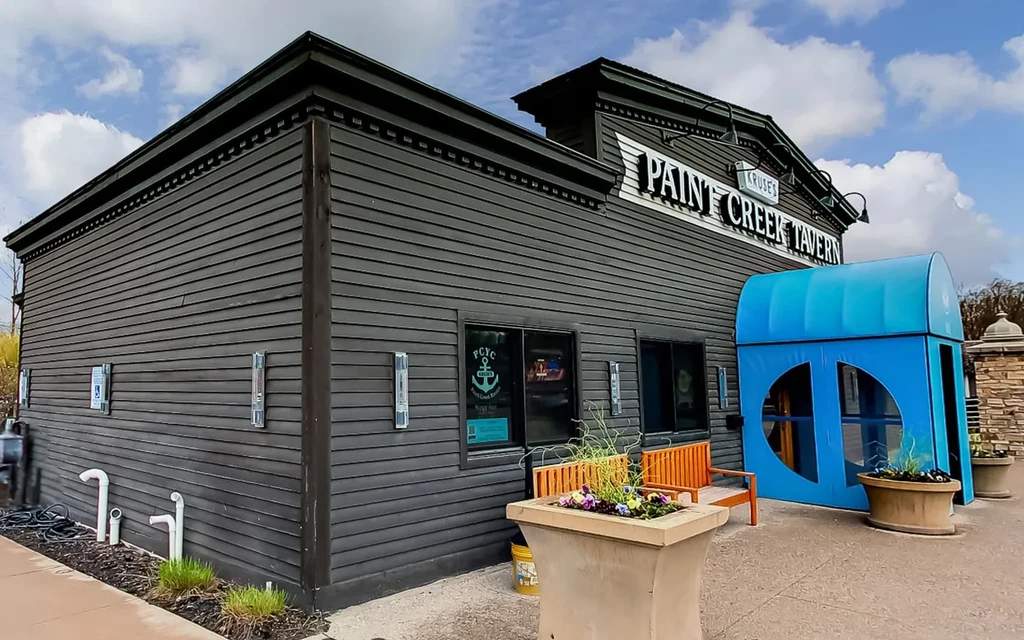 Two-story, dark grey KRUSE'S PAINT CREEK TAVERN with a bright blue archway.